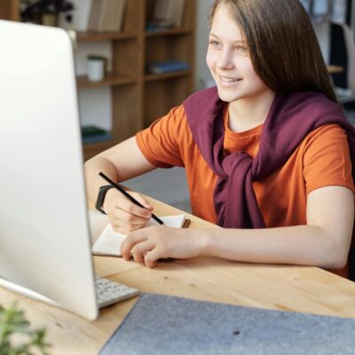 Woman in Orange Shirt Writing on White Paper